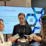 Three representatives discussing EPICURE services at an HPC conference booth with a display screen behind them.
