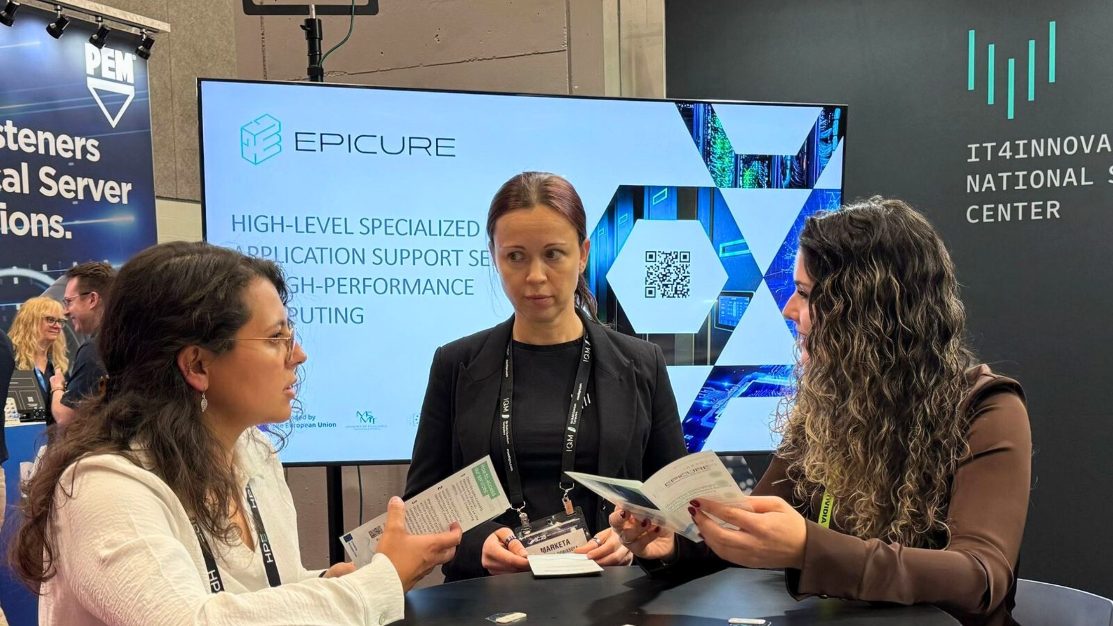 Three representatives discussing EPICURE services at an HPC conference booth with a display screen behind them.