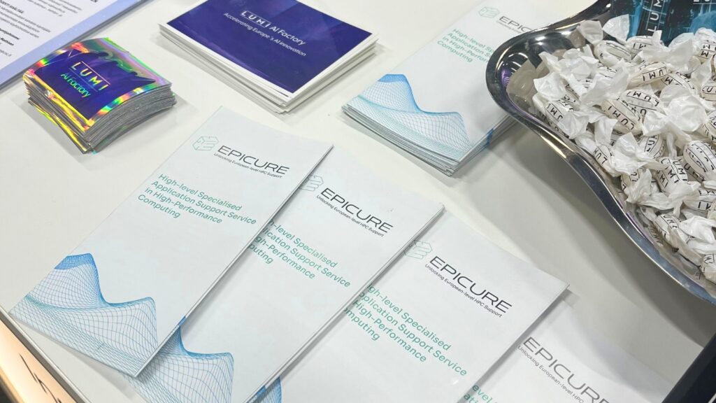 Close-up of a table displaying EPICURE brochures alongside LUMI AI Factory materials and a bowl of wrapped sweets, arranged at an event stand.