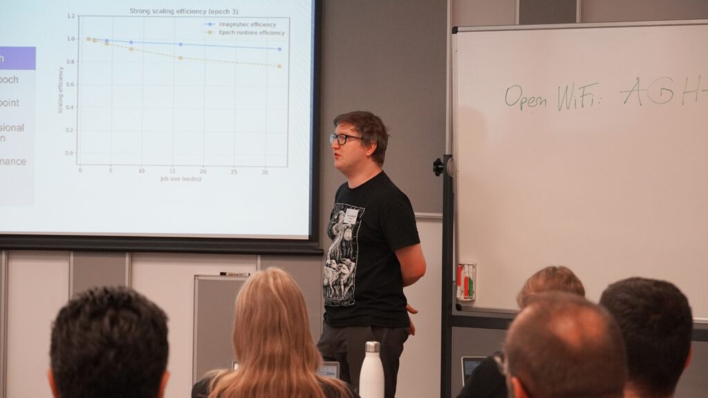 Speaker presenting technical content during a conference session, standing beside a projected chart on scaling efficiency while addressing an audience.