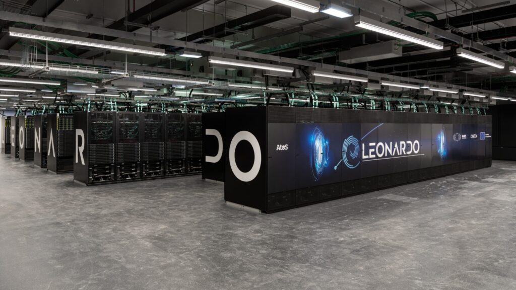 Interior view of the Leonardo supercomputer system, with large black server cabinets, visible cabling overhead, and illuminated branding panels in a modern data centre environment.