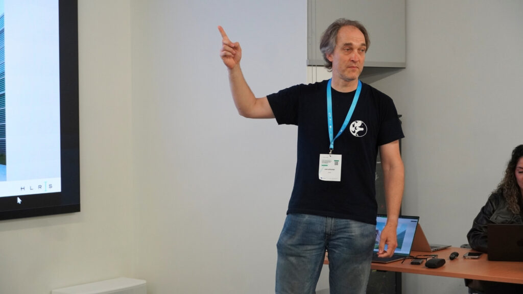 Speaker gesturing while presenting during an HPC workshop session, standing beside a projected slide and addressing participants.