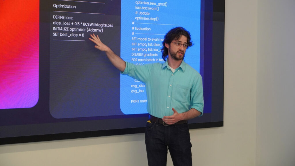 Presenter explaining optimisation steps on a slide during an HPC workshop, gesturing towards code and loss function details.