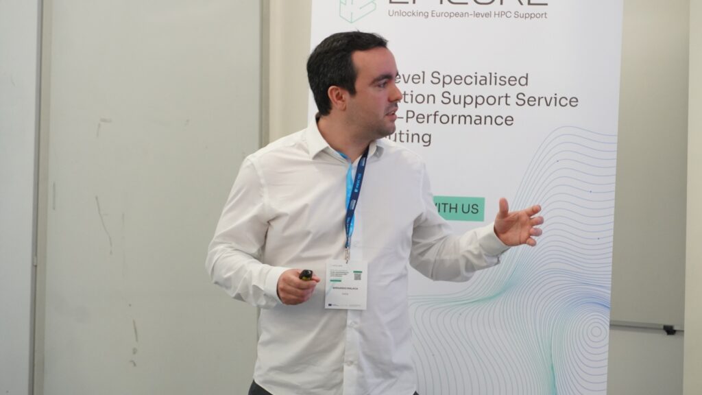 Speaker delivering a presentation beside an EPICURE banner on high-performance computing support, gesturing while addressing an audience.