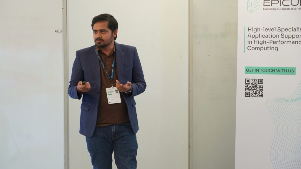 Speaker presenting at an HPC workshop, gesturing while explaining, with an EPICURE banner visible beside him.