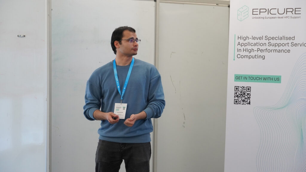 Speaker delivering a presentation beside an EPICURE banner on high-performance computing support, gesturing while addressing an audience.