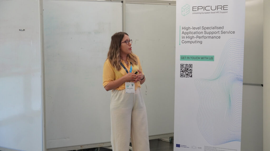 Speaker delivering a presentation beside an EPICURE banner on high-performance computing support, gesturing while addressing an audience.