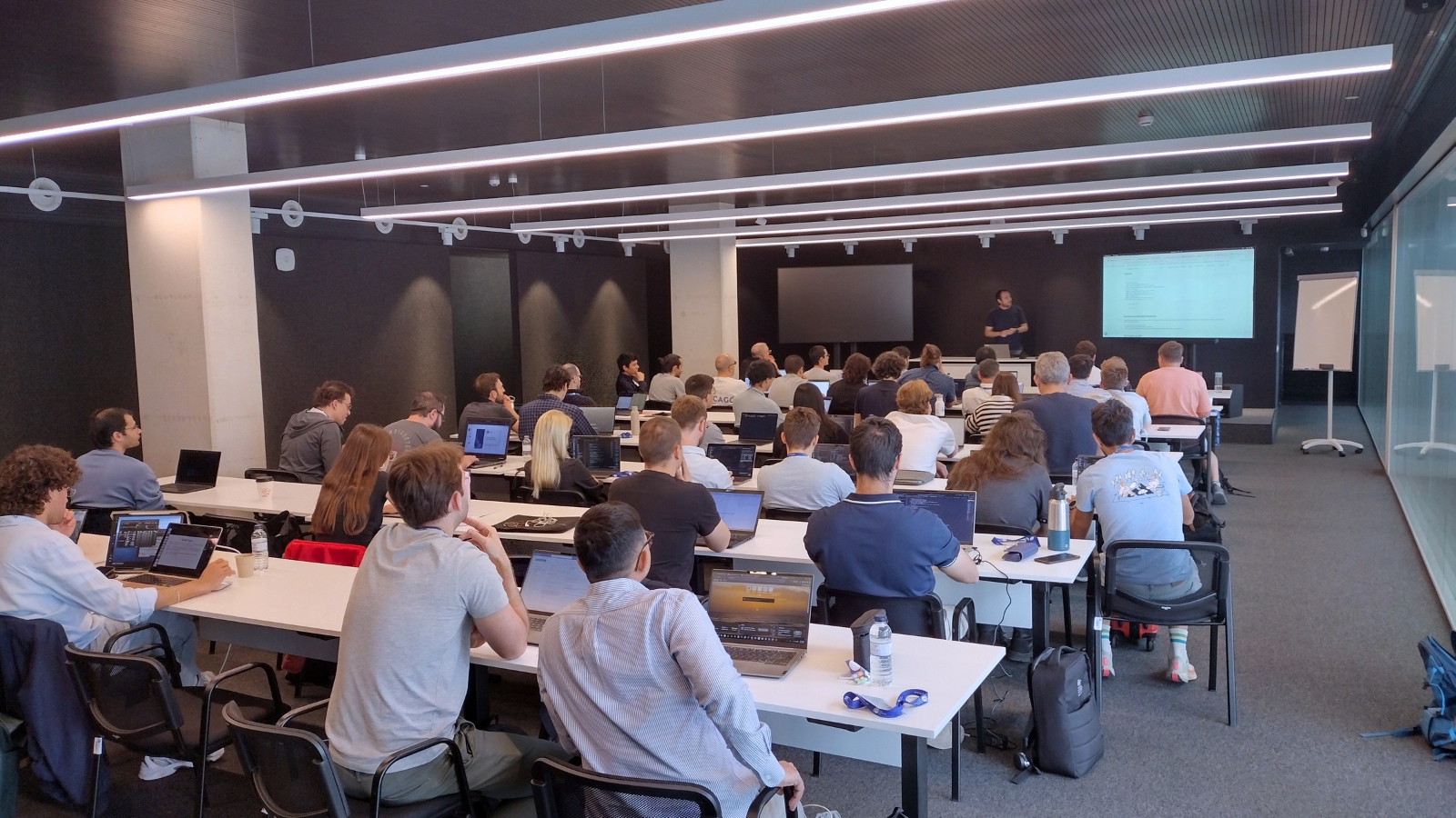 Participants in a modern training room, following a technical presentation on large-scale HPC code optimisation and performance analysis while working on laptops during the hands-on session.