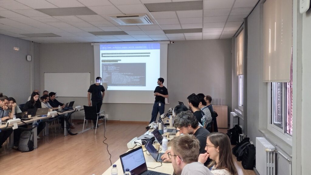 Two presenters explain optimisation examples, while participants work interactively on their laptops during the hands-on session.