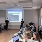 Two presenters explain optimisation examples, while participants work interactively on their laptops during the hands-on session.