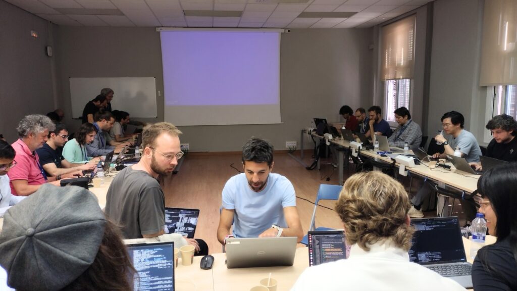 Participants collaborate during a workshop session, working in groups with laptops and code examples in a classroom environment.