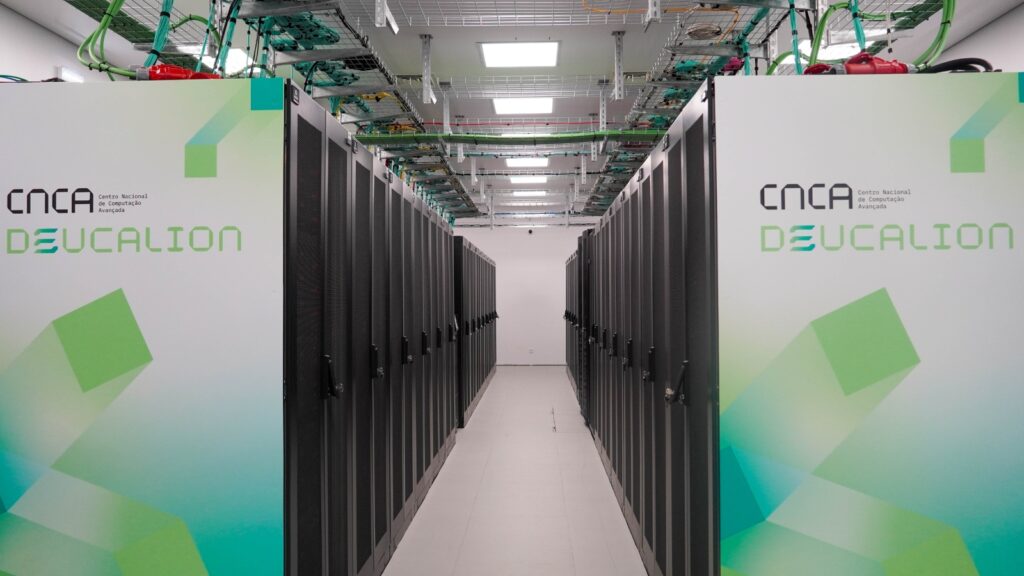 Interior view of the Deucalion supercomputer system, with large black server cabinets, visible cabling overhead, and illuminated branding panels in a modern data centre environment.